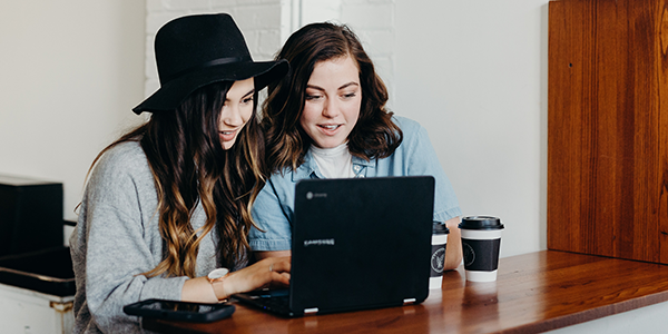 Two women looking at a laptop with coffee sitting on the table.
